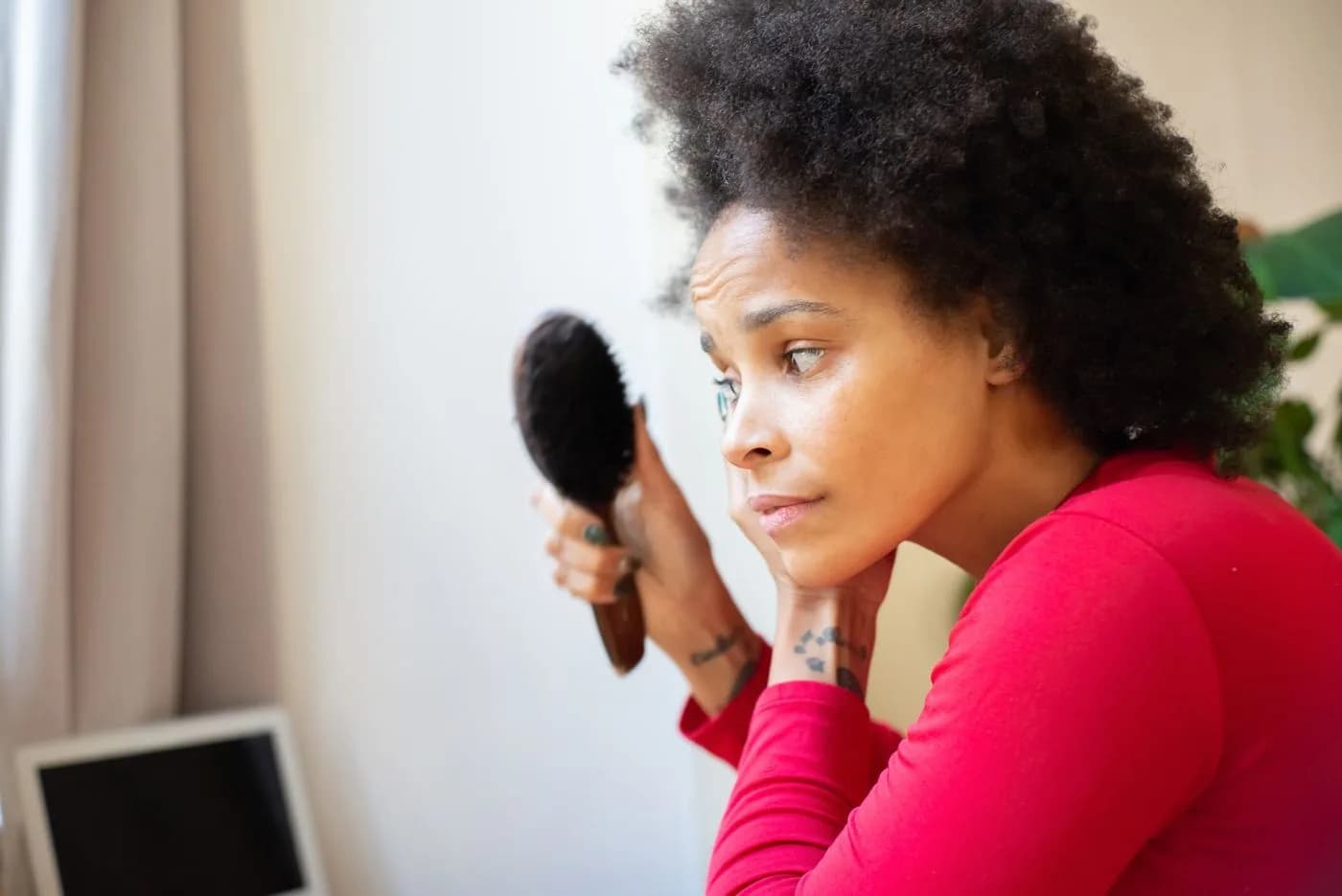 Woman looking with concern at her hairbrush with shed hairs against the light